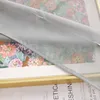A close-up of a sheer gray curtain with a floral pattern visible underneath, framed by a gold border. Produktbild-Vorschau