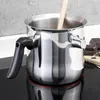A stainless steel pot with a black handle sits on a black stovetop. There is a wooden spoon inside the pot and some chocolate pieces on a cutting board to the right. Produktbild-Vorschau