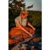 A woman is sitting on the ground in a natural outdoor setting, preparing a sleeping bag. Anteprima dell’immagine prodotto