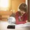 A young girl is lying on the floor reading a book next to a levitating moon lamp. Produktbild-Vorschau