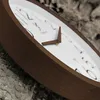 A close-up shot of a wooden wall clock with a white face and brown hands, set against a textured, natural background. Voir les images du produit