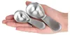 A hand holding two stainless steel measuring spoons. Produktbild-Vorschau