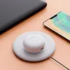 A white wireless charging pad with white earbuds case on top, next to a laptop and a smartphone. Produktbild-Vorschau