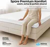 A person sitting on a bed with a white fitted sheet. Produktbild-Vorschau