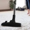 A vacuum cleaner head on a white carpet with a person's legs in the background. Produktbild-Vorschau