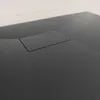 A close-up view of a black shower tray with a drain cover. Produktbild-Vorschau