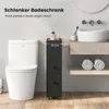 A slim bathroom cabinet is shown next to a toilet, with a sink and towels in the background. Náhled obrázku produktu
