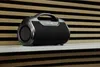 A black and gray Bluetooth speaker sits on a white shelf in front of a slatted wood background. Anteprima dell’immagine prodotto