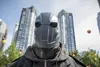 A person wearing a dark grey mask and jacket stands in front of tall buildings. Podgląd zdjęcia produktu