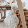 A close-up shot of a woven basket with a wooden handle and a tassel hanging from it, with shelves of items in the background. Anteprima dell’immagine prodotto