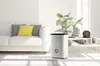 A white humidifier is placed on a wooden floor next to a white sofa in a bright, modern living room. Produktbild-Vorschau