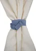 A close-up of a cream-colored curtain or fabric being held together by a blue fabric tie. Náhled obrázku produktu