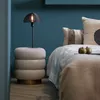A bedside table with a lamp and two apples next to a bed with pillows and a blanket. Produktbild-Vorschau