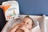 A baby is lying on a changing table next to a package of disposable underpads. Voir les images du produit