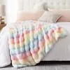 A fluffy, rainbow-colored blanket is draped over a bed with white bedding and pillows. Produktbild-Vorschau