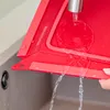 Water is being poured onto a red foldable baking dish over a sink. Produktbild-Vorschau