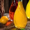 Three glass bottles filled with colored liquids, a lemon, and some straw on a wooden surface. Podgląd zdjęcia produktu