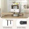 A bedside table with a drawer and open shelf, placed next to a sofa. A robot vacuum cleaner is shown underneath the table. Podgląd zdjęcia produktu