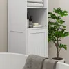 A white bathroom cabinet with shelves and a closed cabinet door, next to a bathtub and a potted plant. Produktbild-Vorschau
