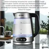 A glass electric kettle with a stainless steel base and handle is shown on a kitchen counter, with a blurred background of a window and greenery. Náhľad obrázku produktu