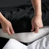 Hands are shown tucking a black fitted sheet onto a mattress. Produktbild-Vorschau