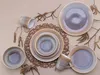 A collection of stoneware plates and mugs with a speckled, iridescent glaze, arranged on a neutral background with decorative branches. Náhľad obrázku produktu