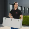 A man is carrying a silver case in front of a modern building. Produktbild-Vorschau