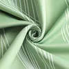 A close-up shot of green fabric with a white water wave pattern, folded into a swirl. Produktbild-Vorschau