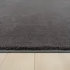 A close-up view of the edge of a dark gray rug on a light wood floor. Produktbild-Vorschau