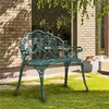 A vintage-style green metal garden bench with a rose pattern sits on a grassy lawn in front of a brick building. Podgląd zdjęcia produktu