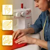 A woman is sewing on a white sewing machine, with three informational icons on the left side. Podgląd zdjęcia produktu