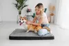 A woman petting a corgi dog on a dog bed in a bright, modern room. Produktbild-Vorschau