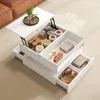 A white lift-top coffee table with multiple storage compartments is shown in a living room setting, with a brown sofa visible in the background. Produktbild-Vorschau