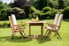 A wooden garden table and chairs set on a lush green lawn with trees and bushes in the background. Produktbild-Vorschau