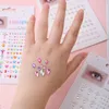A person's hand with various colorful rhinestones applied to it, surrounded by packaging for the rhinestones. Produktbild-Vorschau