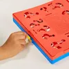 A child's hand is shown interacting with a red and blue board game, possibly a guessing game, with question mark cutouts. Anteprima dell’immagine prodotto