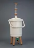 A beige Bokashi composter with a green spigot and brown legs, set against a plain gray background. Náhled obrázku produktu