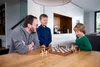 A father and two sons are playing chess at a wooden table in a modern home. Podgląd zdjęcia produktu