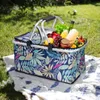 A picnic basket filled with food and drink is placed on a blanket in a grassy outdoor setting. Náhled obrázku produktu