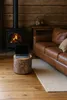 A cozy living room scene with a fireplace, a leather sofa, and a laptop on a tree stump side table. Podgląd zdjęcia produktu