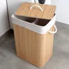 A bamboo laundry basket with a lid and fabric lining, placed on a floor next to a washing machine. Náhled obrázku produktu