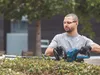 A man is using a hedge trimmer to trim a bush. Produktbild-Vorschau