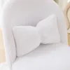 A close-up of a white fluffy chair with a bow-shaped pillow. Podgląd zdjęcia produktu