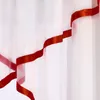 A close-up view of a white sheer curtain with a red satin ribbon trim. Produktbild-Vorschau