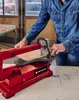 A person is using a red jigsaw to cut a piece of wood in a workshop. Produktbild-Vorschau