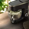 A close-up shot of a black stand mixer with a metal bowl and a clear splash guard, on a wooden table. Náhľad obrázku produktu