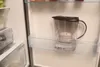 A water filter pitcher placed on a shelf inside an open refrigerator. Produktbild-Vorschau