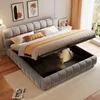 A modern bedroom with a gray upholstered bed frame featuring a lift-up storage mechanism, displaying bedding and pillows. Artwork hangs on the wall, and a bedside table with a lamp is visible. Anteprima dell’immagine prodotto
