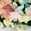 A close-up of a decorative pink glitter bird ornament with pink feathers, placed on a Christmas tree with other ornaments and poinsettia decorations. Náhľad obrázku produktu