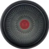 The bottom of a black frying pan with a red circular logo in the center and radiating white lines. Voir les images du produit